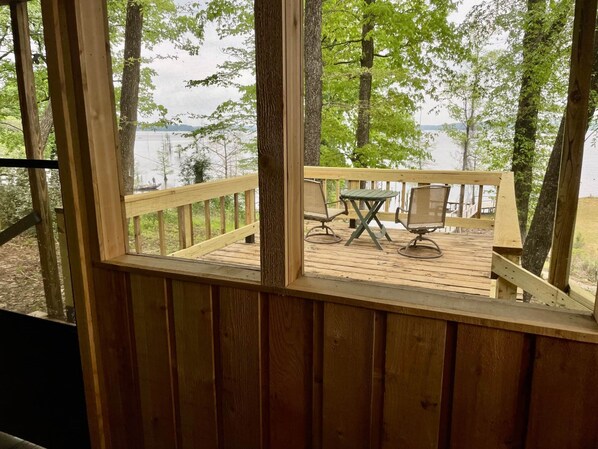 A wooden deck with a table and chairs, overlooking a lake surrounded by trees. - D'Arbonne Nest Rentals: The Pelican's Nest (Union Parish)