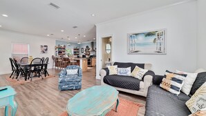 A spacious living room with a dining area, a kitchen in the background, and a large window with a beach view. - Seaclusion (Gulf Shores)