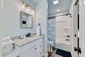 A bathroom with a marble countertop, white cabinets, a large mirror, a shower with a curtain, and a toilet. - Seaclusion (Gulf Shores)