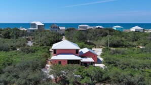 A coastal property with multiple houses, a prominent pink house with a white roof, and a view of the ocean. - Seaclusion (Gulf Shores)