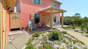 A pink house with a covered porch, outdoor seating, and a garden area. - Seaclusion (Gulf Shores)