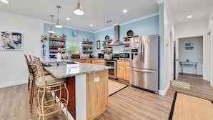 A modern kitchen with wooden cabinets, stainless steel appliances, and a central island with bar stools. - Seaclusion (Gulf Shores)