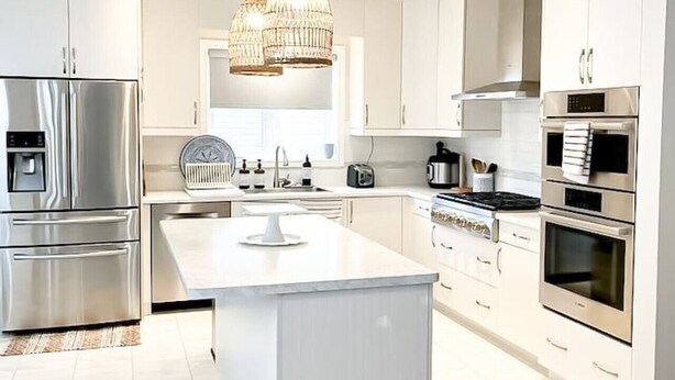 Une cuisine moderne dotée d’appareils électroménagers en acier inoxydable, d’un îlot central et de luminaires suspendus.