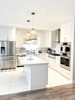 A modern kitchen with stainless steel appliances, a central island, and pendant lighting. - Luxury Boho Escape - 2.5 Baths, 4 Beds, 2 King Suites - 15 min to Falls and NOTL (Thorold)