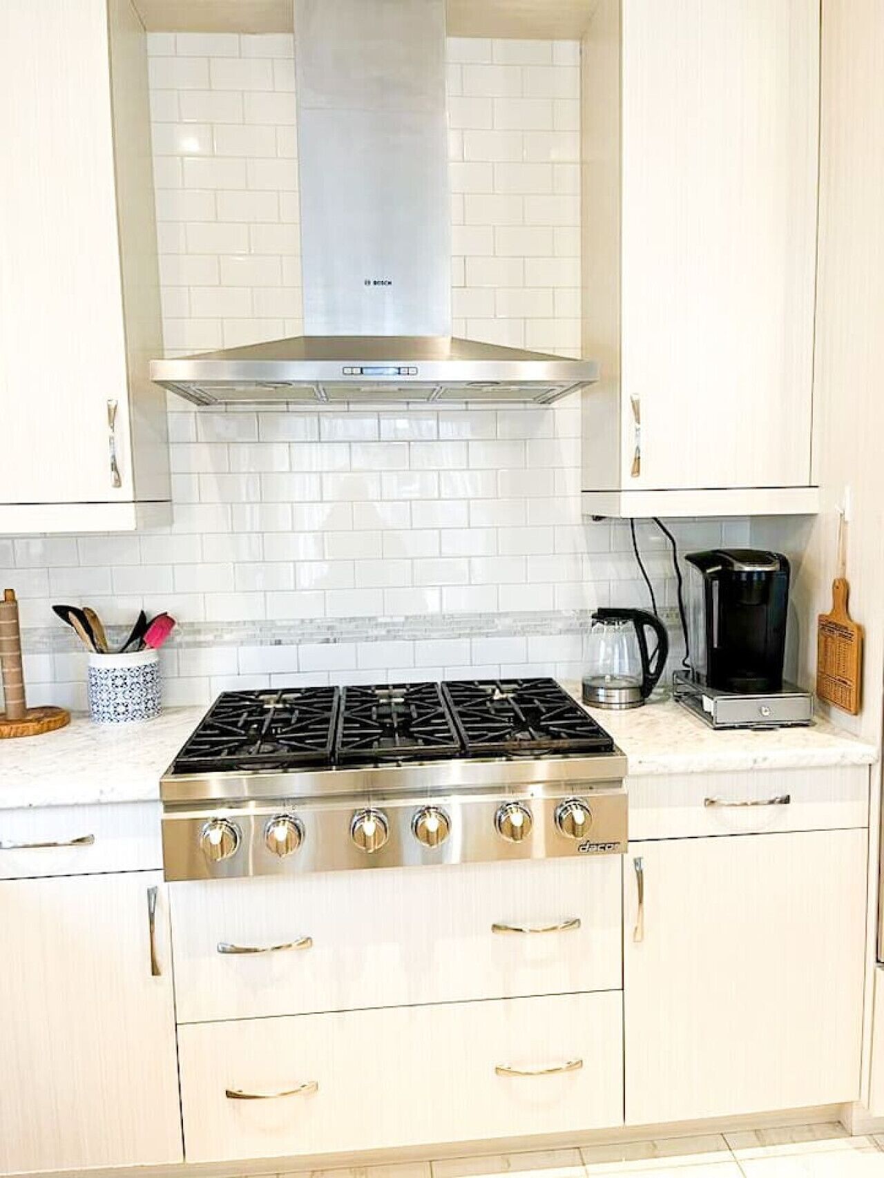 Una cocina con armarios blancos, estufa de acero inoxidable y cafetera.