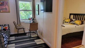 A compact room with a bed, a desk, and a chair. There is a window with a view of greenery outside. - Private Charming Garden Guest Suite Presidio Hts. (San Francisco)