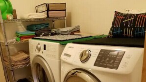 A laundry area with two front-loading washing machines, a metal shelf with folded clothes, and a green water bottle. - Private Charming Garden Guest Suite Presidio Hts. (San Francisco)