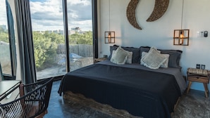 A bedroom with a large bed, two bedside tables, a wall-mounted crescent moon decoration, and a view of greenery outside.