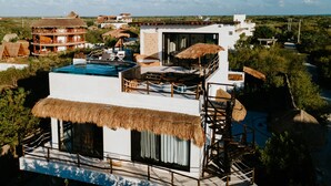 Un hotel moderno con piscina en la azotea, construcciones con techo de paja y vistas panorámicas del paisaje circundante.