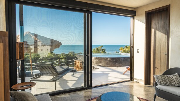 Una habitación moderna con un amplio ventanal corredera que da a un balcón con vistas al océano.