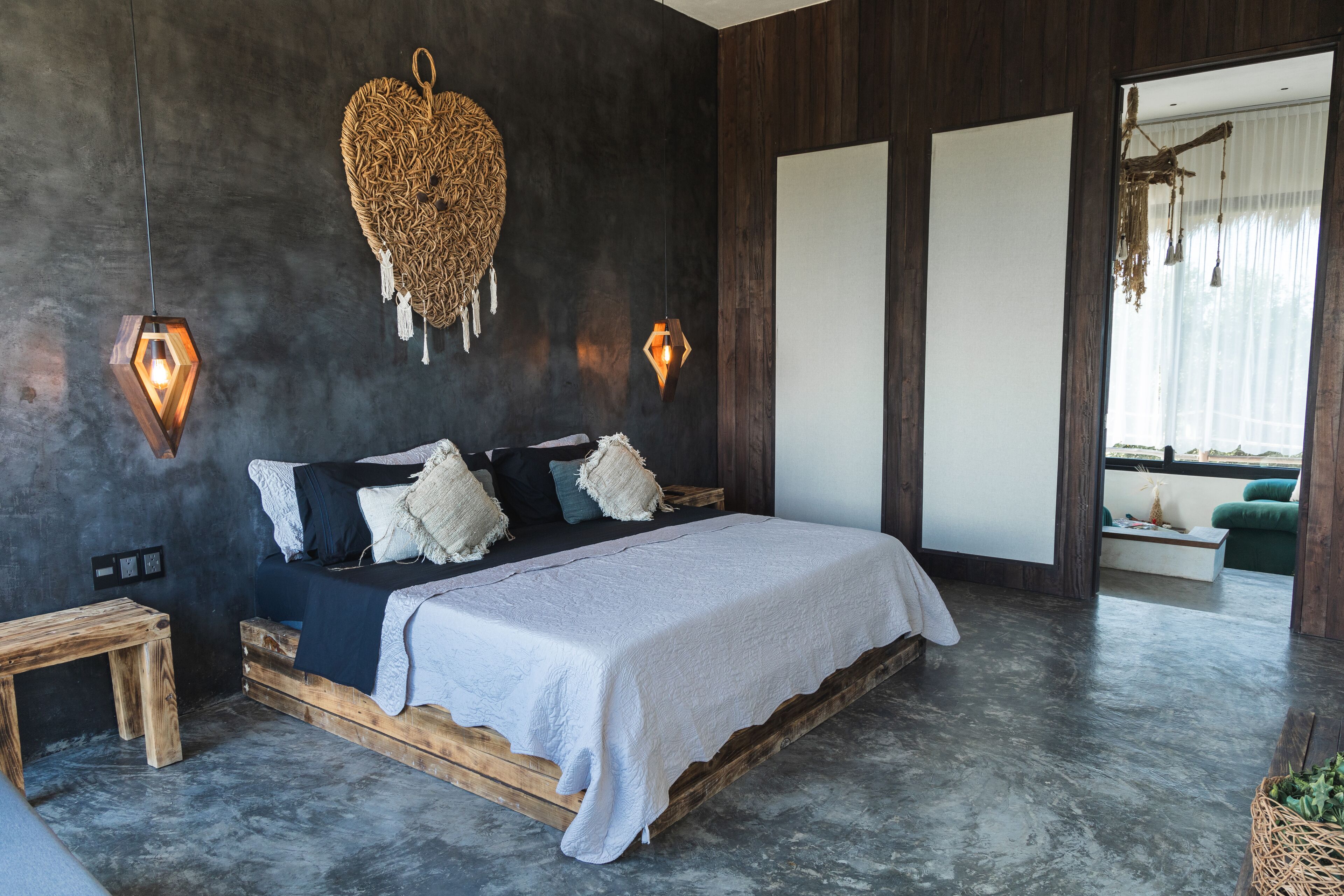 A modern bedroom with a wooden bed, a woven wall hanging, and a hanging light fixture.