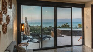 Una sala de estar moderna con un gran ventanal corredera que da a un balcón con vistas al océano.