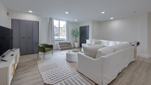 Een moderne woonkamer met een bank, een televisie, een groene fauteuil en een trap die naar een ander niveau leidt.