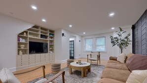 A living room with a sofa, ottomans, a coffee table, a TV, and built-in shelving. - Central Luxury 3-Level Home - Rooftop + Garage (Lancaster)