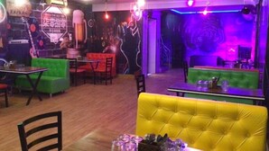 A restaurant interior with green and yellow booths, tables with cutlery, and a neon sign. - Hotel Bhullar (Amritsar)