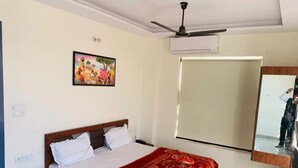 A bedroom with a bed, a ceiling fan, an air conditioning unit, a mirror, and a wall-mounted TV. - Hotel Bhullar (Amritsar)