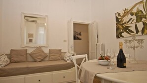 A room with a sofa bed, a dining table with a bottle of wine, and a mirror on the wall. - Penthouse Alisa - Penthouse Alisa (Rome)