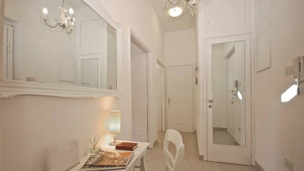 A room with a white desk, a chair, a lamp, a mirror, and a chandelier. - Penthouse Alisa - Penthouse Alisa (Rome)