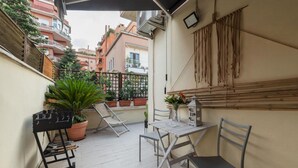 A small outdoor patio with a table and chairs, a barbecue grill, potted plants, and a view of neighboring buildings. - Penthouse Alisa - Penthouse Alisa (Rome)
