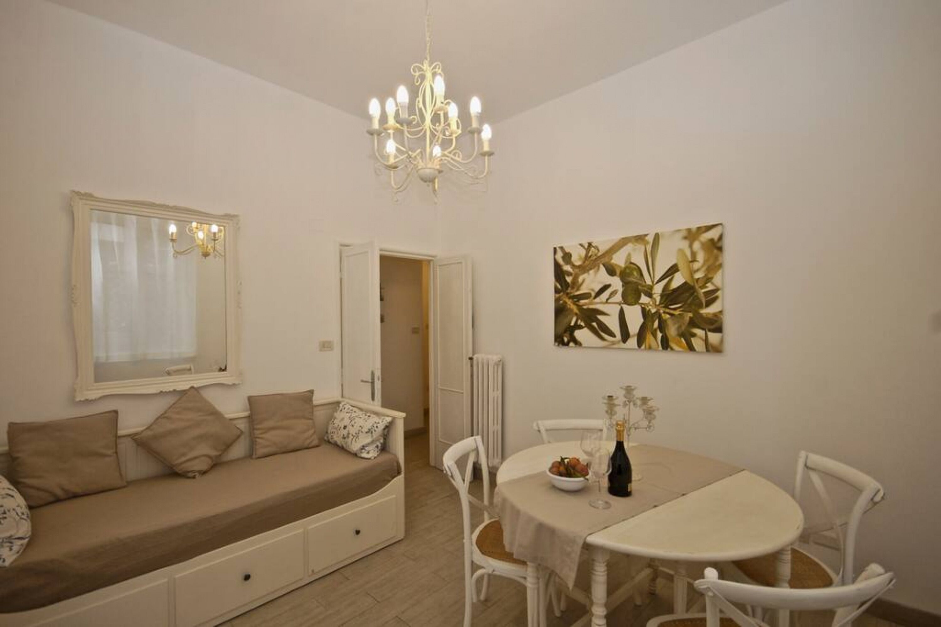 A cozy room with a sofa, a dining table, chairs, a chandelier, and a window with curtains.