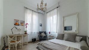 A bedroom with a bed, a desk, a chair, a TV, and a chandelier. - Penthouse Alisa - Penthouse Alisa (Rome)