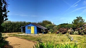 A small blue house with a yellow door, surrounded by a garden with various plants and flowers. - Simple Bonheur (Penvénan)