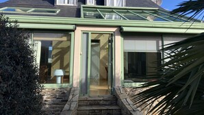 A house with a sloped roof, a green-framed conservatory, and a stone staircase leading to the entrance. - Simple Bonheur (Penvénan)