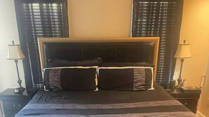 Een groot bed met hoofdeinde, twee nachtkastjes met lampen, en een klein tafeltje met afstandsbediening ervoor.
