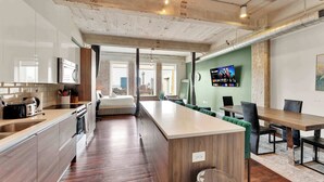 A modern kitchen with a large island, a dining area with green upholstered chairs, and a TV mounted on the wall. - Downtown Dallas 3BR Home | Pool, Gym & Oasis (Dallas)