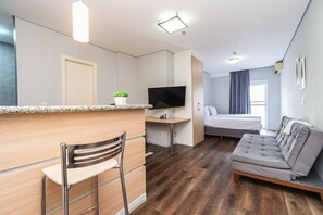 Habitación de hotel compacta con kitchenette, cama, zona de estar y televisión.