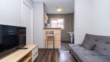 A compact living space with a television, a sofa, a kitchen area, and a window.
