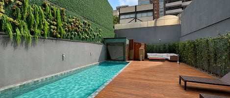 Ein Poolbereich auf dem Dach mit Holzterrasse, einer begrünten Wand und Blick auf umliegende Gebäude.