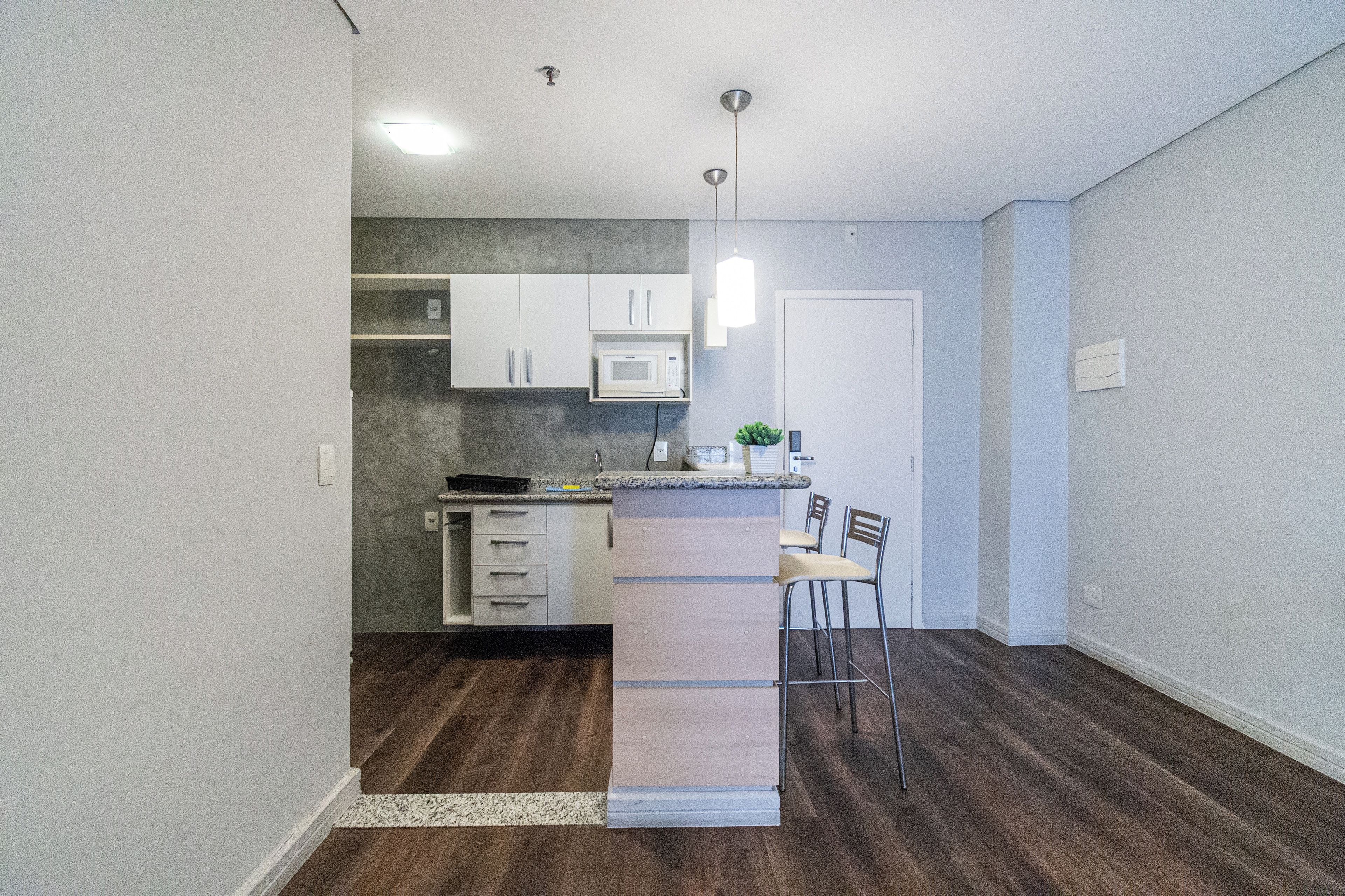 A compact kitchen with a microwave, a small island with bar stools, and a door leading to another room.