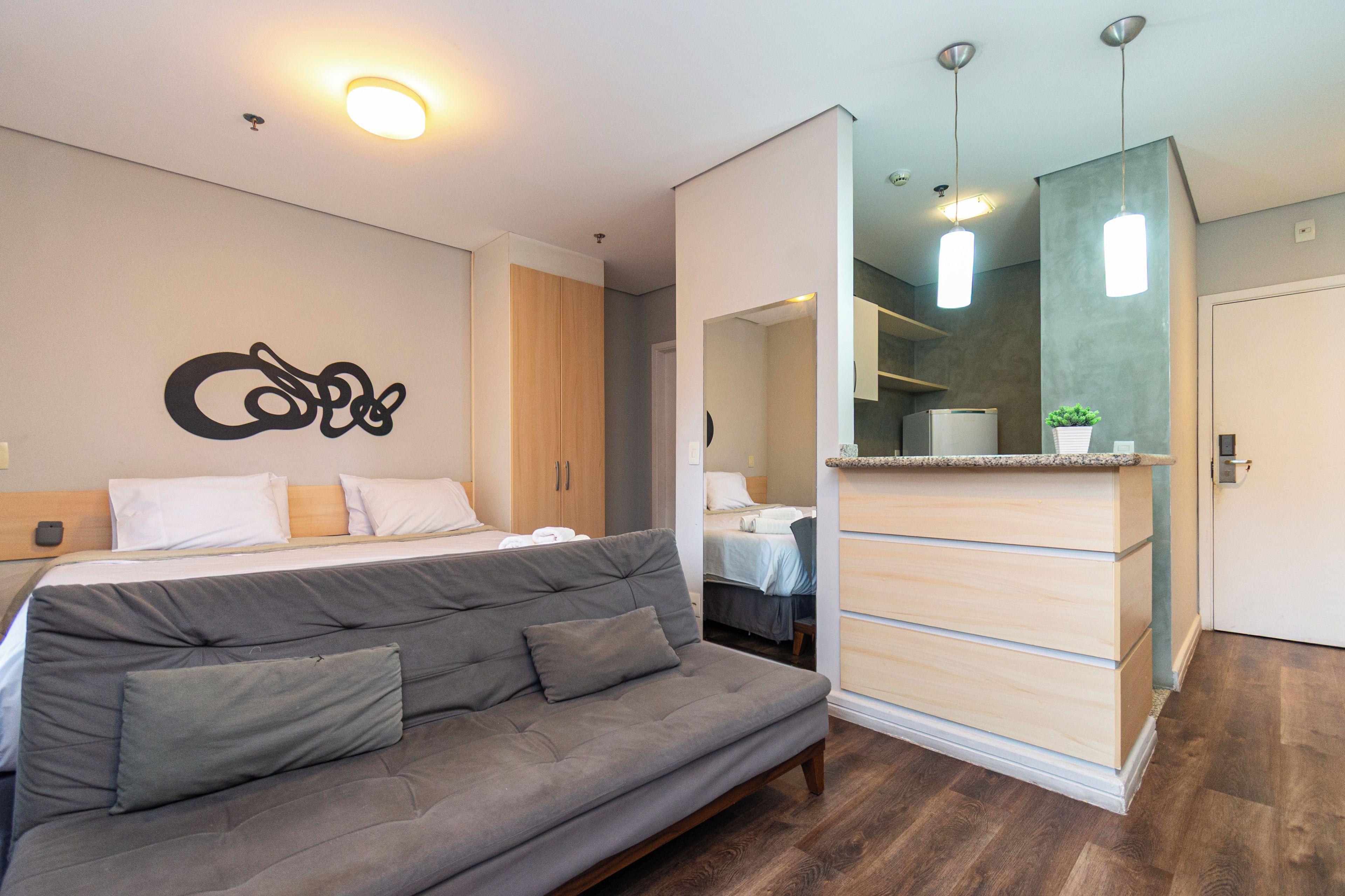 Una habitación de hotel moderna con cama, sofá, espejo y kitchenette.