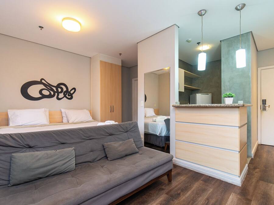 Een moderne hotelkamer met een bed, een bank, een spiegel en een kitchenette.
