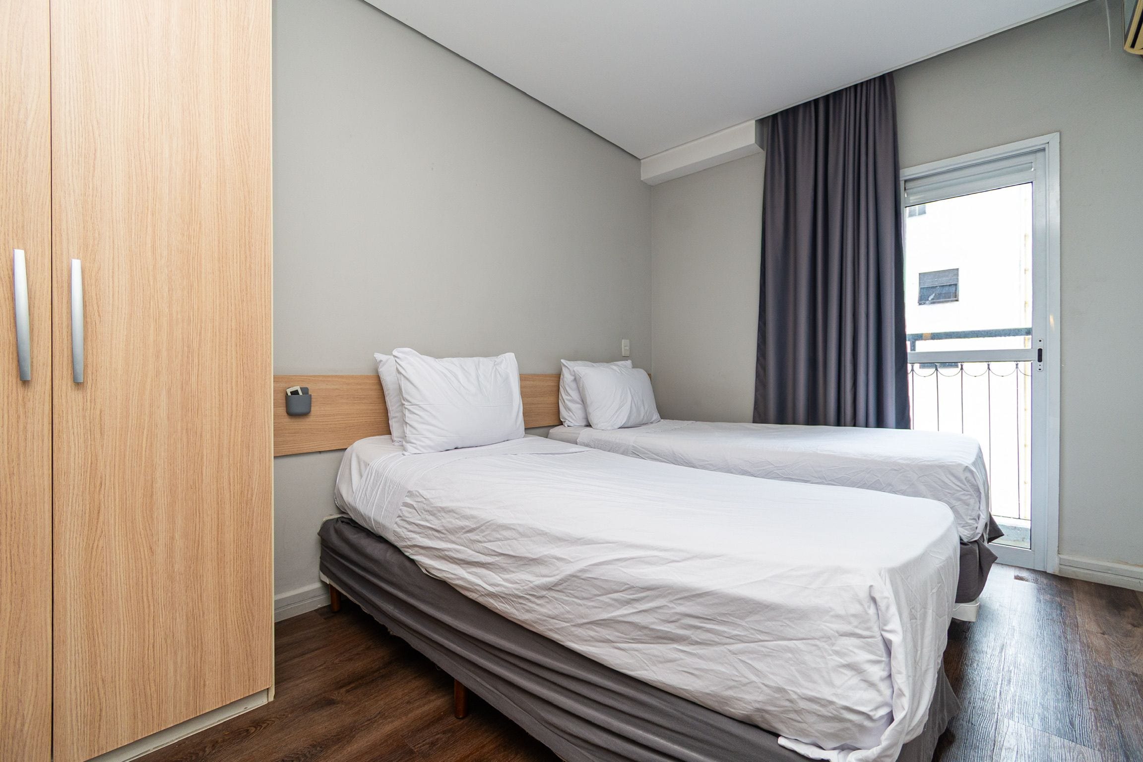 Een hotelkamer met twee bedden, een garderobe en een raam met gordijnen.