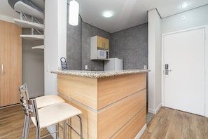 Una cocina moderna con encimera de madera, microondas y refrigerador. Hay un taburete de bar y una puerta a la derecha.