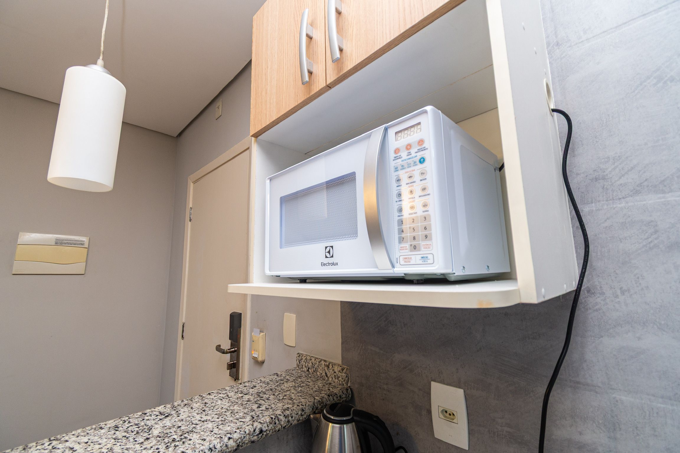 Cozinha com micro-ondas numa prateleira, chaleira e bancada.