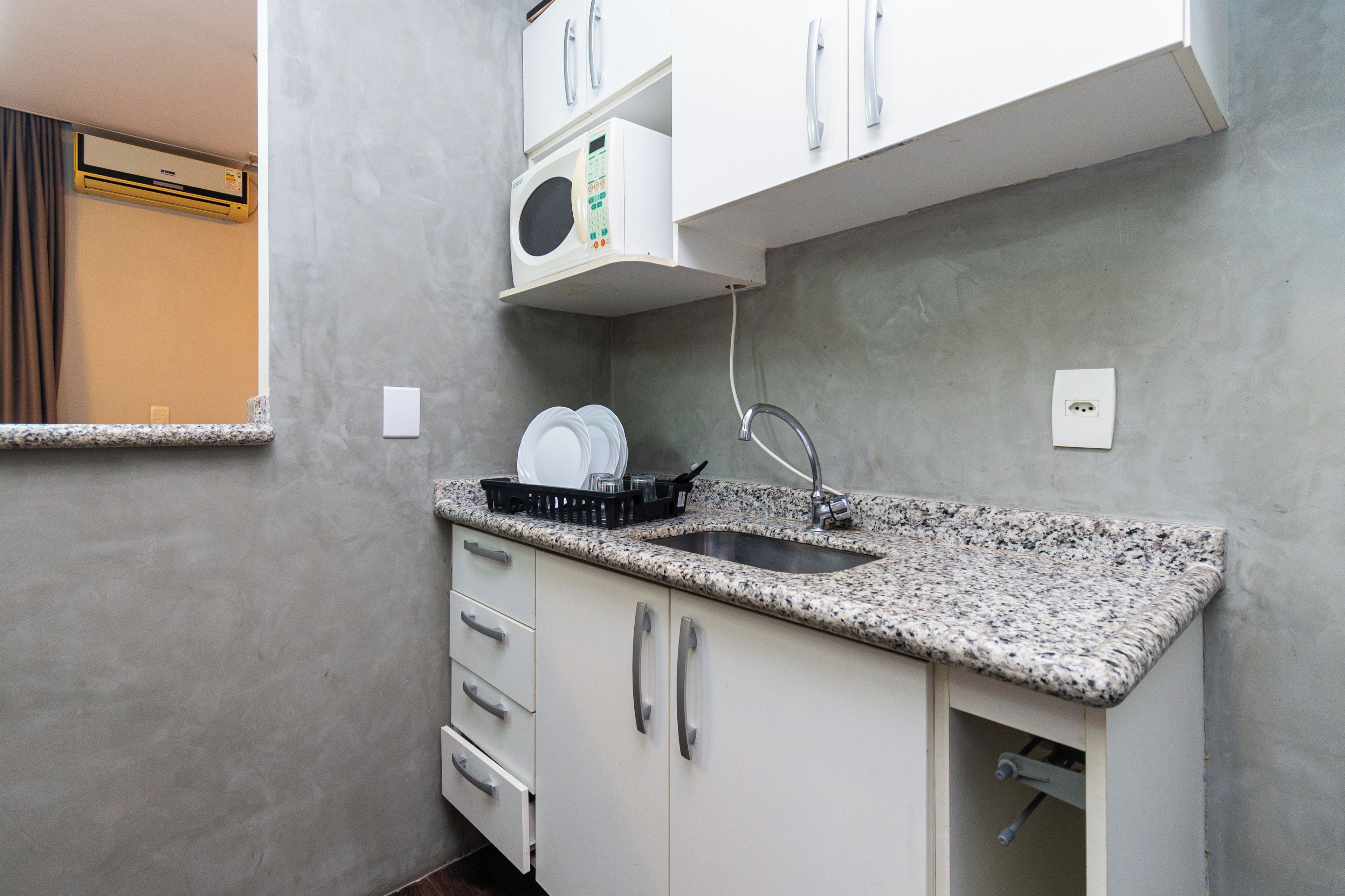 A compact kitchen with a granite countertop, white cabinets, a built-in microwave, and a stainless steel sink.