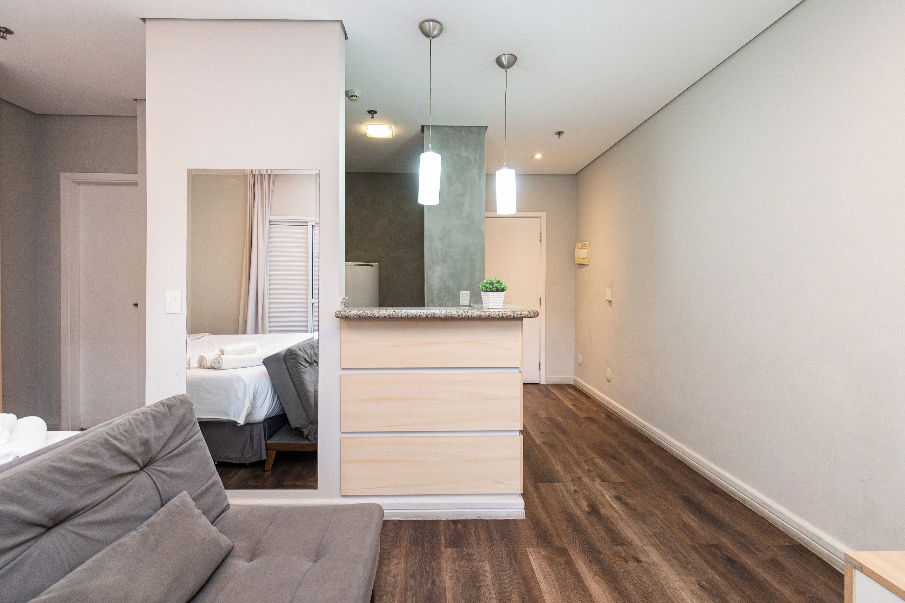 A modern hotel room with a grey sofa, a small kitchenette, and a wooden floor.