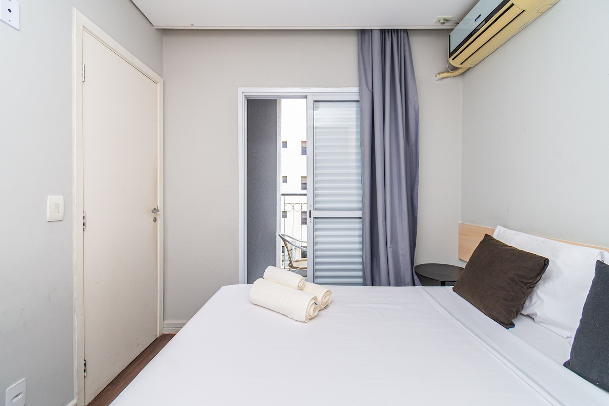 Une chambre d’hôtel avec un lit, une chaise, une petite table et une fenêtre avec des rideaux.