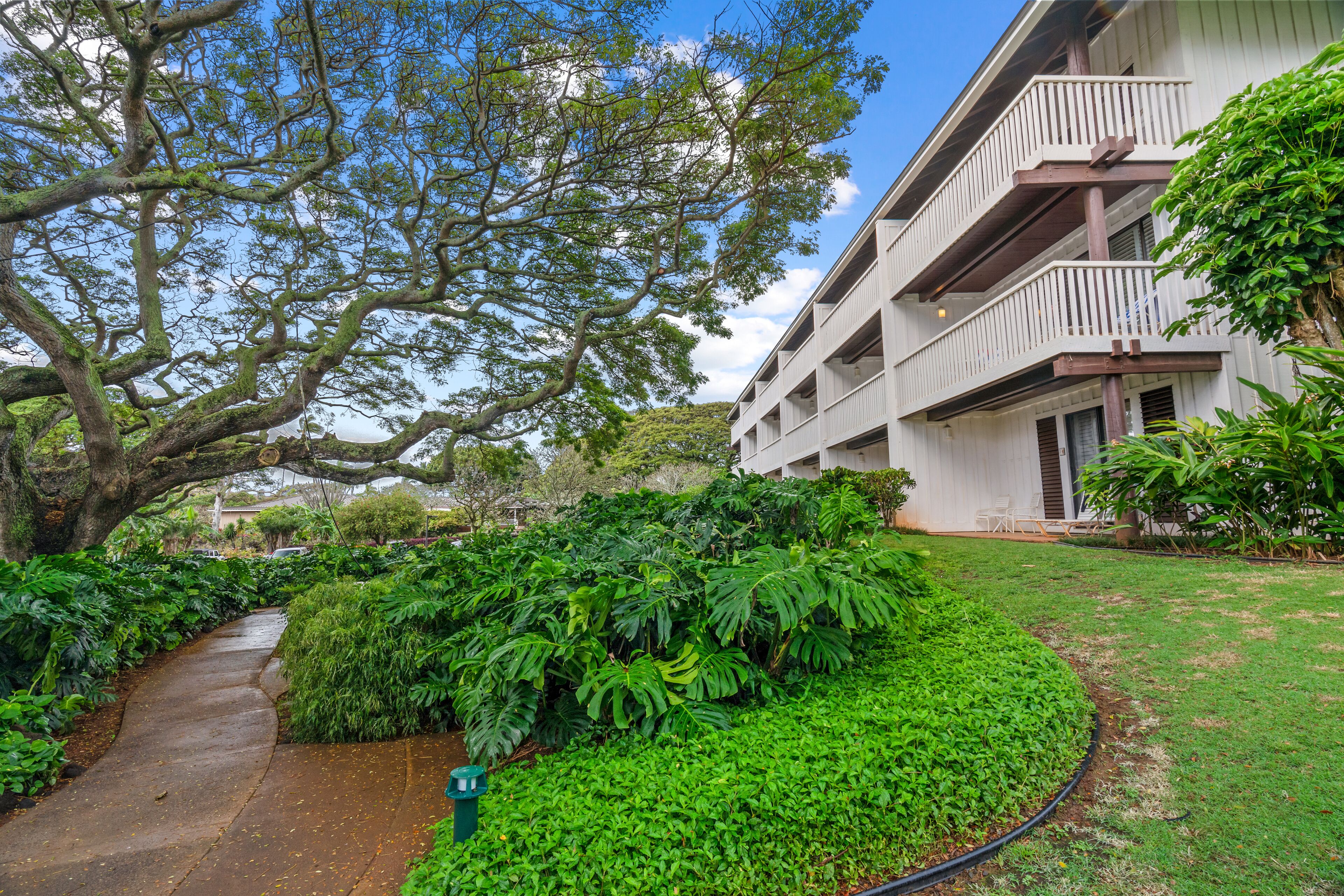 A building with a white exterior, a balcony, and a well-maintained garden with various plants and a curved pathway.