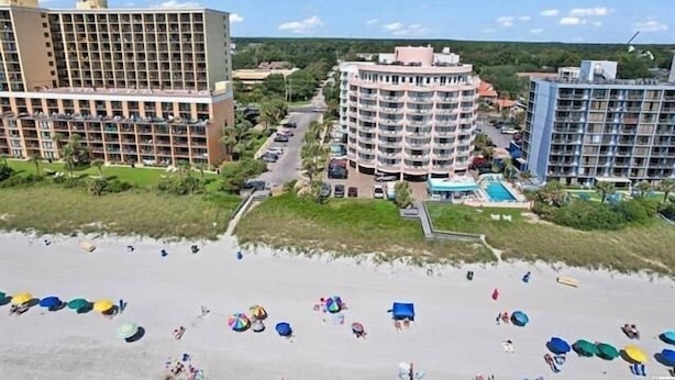 Et strandhotel med flere balkoner, en swimmingpool og et strandområde med parasoller.