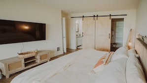Un dormitorio con una cama grande, un televisor montado en la pared, un aparador de madera y un armario con puertas correderas.