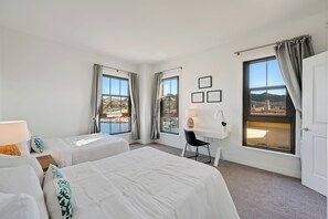 Ein Hotelzimmer mit zwei Betten, einem Schreibtisch und großen Fenstern mit Blick auf das Meer und die Hügel.
