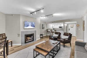 A modern living room with a fireplace, a television mounted on the wall, and a dining area with a wooden table and chairs.