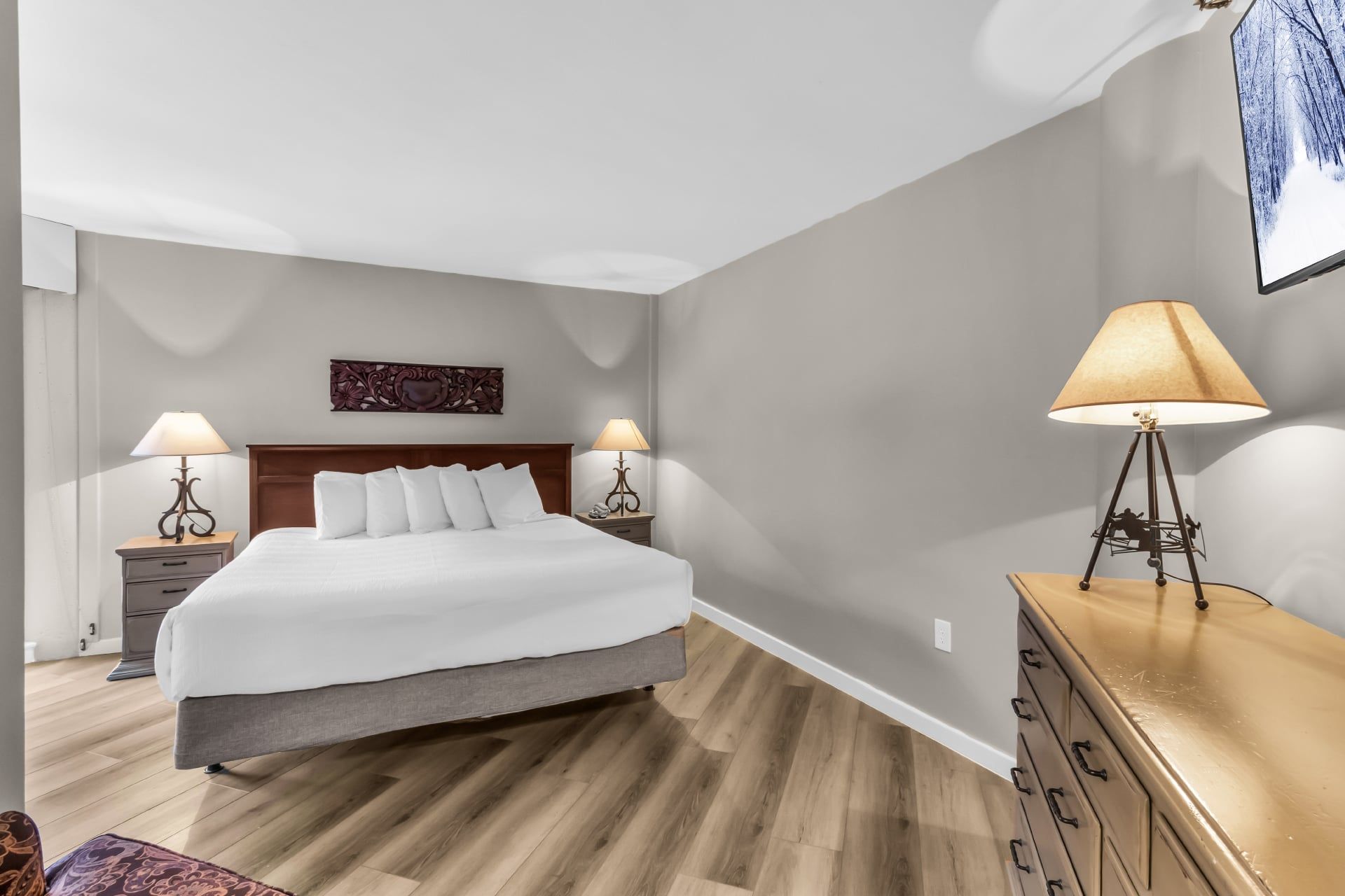 Habitación de hotel con una cama, dos mesitas de noche con lámparas, un aparador y una obra de arte colgada en la pared.