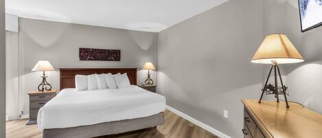Habitación de hotel con una cama, dos mesitas de noche con lámparas, un aparador y una obra de arte colgada en la pared.