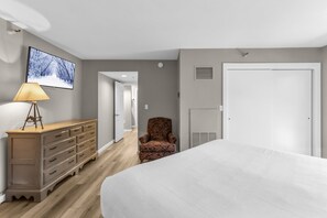 Een slaapkamer met een bed, een dressoir, een stoel, een televisie en een deur.
