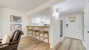 Cocina moderna con armarios blancos, una barra de madera y un comedor con sofá de cuero marrón y sillas de madera.